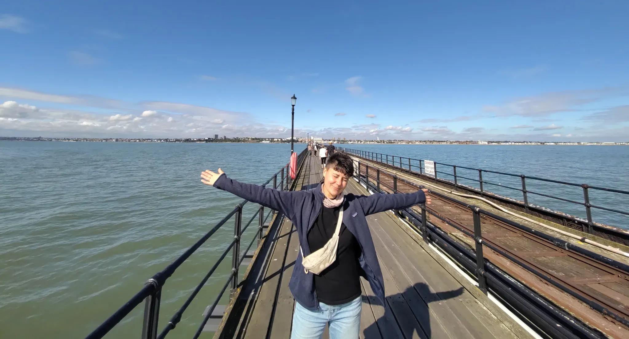 Chiara steht mit ausgebreiteten Armen auf einem Steg, der über eine Meile lang ist. Im Hintergrunde sieht man, weit weg, die Stadt Southend-on-Sea.