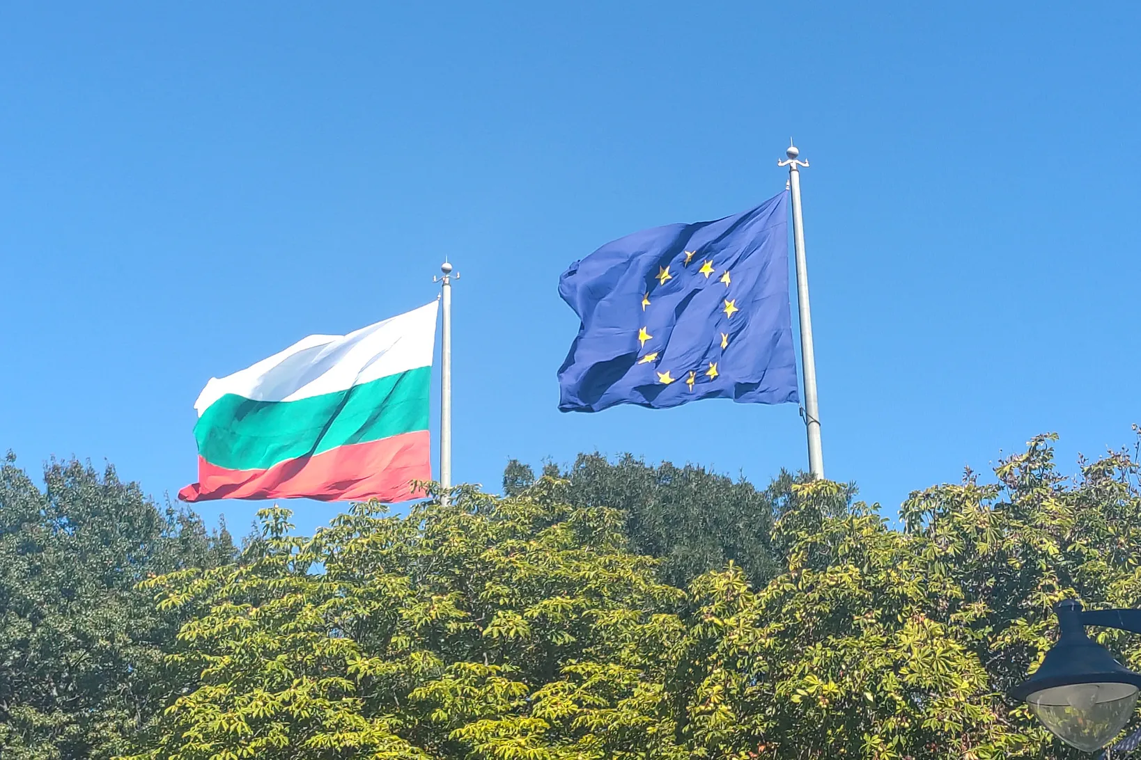 Die bulgarische- und Europa-Flagge wehen über den Wipfeln des Parks Seite an Seite im Wind.